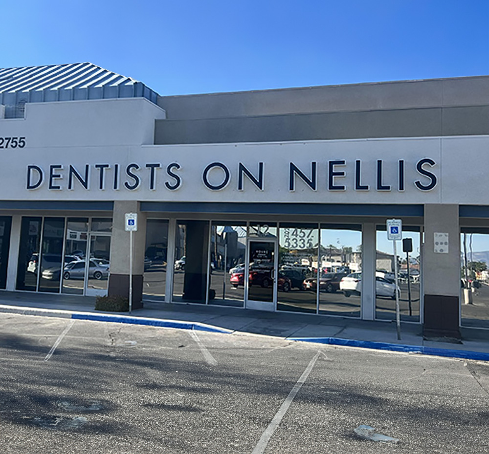 The image shows a sign for Dentists on Nellis in front of a building with a parking lot.